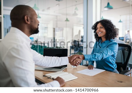 Smiling African American manager sitting at his desk in an office shaking hands with a job applicant after an interview