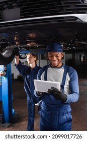 Smiling african american mechanic in gloves using digital tablet in car service