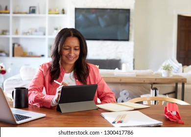 Smiling African American Middle Aged Woman Sitting At A Table Drawing On A Tablet Computer With A Stylus, Front View