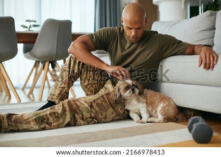 Smiling African American military man cuddling his dog at home.