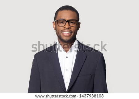 Smiling african American millennial businessman in glasses isolated on grey studio background posing, satisfied successful black male in formal suit wearing spectacles look at camera laughing