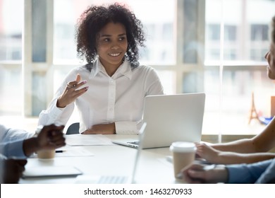 Smiling African American Millennial Businesswoman Hold Company Team Meeting Speak Share Ideas With Colleagues, Young Black Female CEO Talk Negotiate With Employees At Briefing In Boardroom