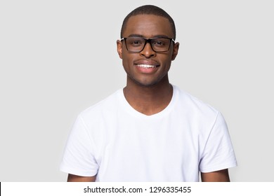 Smiling African American Millennial Casual Man Wearing White T-shirt And Glasses Looking At Camera Isolated On Blank Grey Studio Background, Charming Young Black Single Male Guy Posing For Portrait