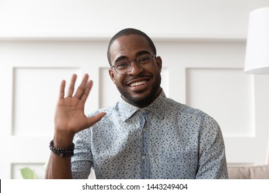 Smiling african American millennial man in glasses look at camera waving saying hello talking on video call, happy black male vlogger in spectacles greeting with subscribers shooting video blog - Powered by Shutterstock