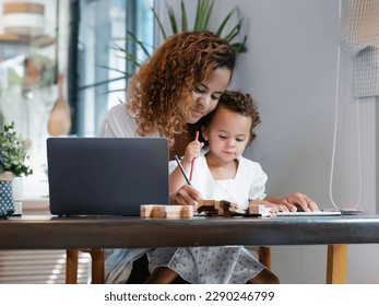 Smiling African American mom working with laptop computer while sitting wooden table in kitchen and playing with her baby girl. Young Black mother do freelance the desk with toddler child at home. - Powered by Shutterstock