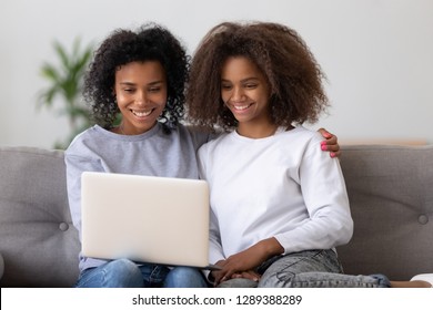 Smiling African American Mother And Daughter Sit On Couch Watching Video On Laptop, Black Millennial Nanny Hang Out With Teen Girl, Relax On Sofa Using Computer, Mom And Kid Rest Together At Home