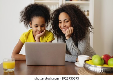 Smiling african american mother with her daughter using laptop in the kitchen at home.