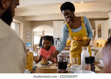 Smiling african american mother serving pancakes to daughter sitting at dining table. Unaltered, lifestyle, family, love, togetherness, childhood, food, breakfast and home concept. - Powered by Shutterstock