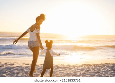 Smiling african american mother walking with cute little girl at beach. Lovely black woman holding hands with little daughter while running towards ocean at beach during sunset with copy space. - Shutterstock ID 2151833761