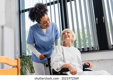 Smiling african american nurse looking at senior patient in wheelchair in hospital - Powered by Shutterstock