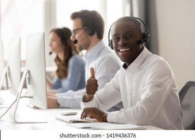 Smiling African American Operator In Headset Look At Camera Show Thumb Up Working On Pc In Shared Office, Happy Black Call Center Agent Or Telemarketer Recommend Customer Service Or Helpdesk