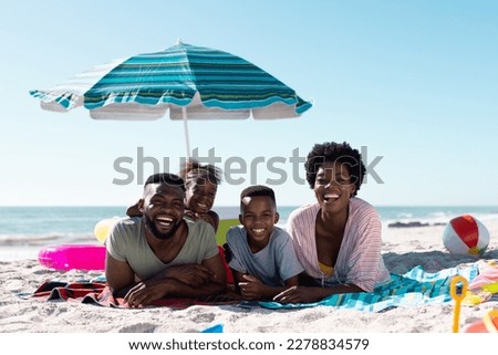 Smiling african american parents and children lying on towels at sandy beach under clear sky. Copy space, unaltered, family, together, parasol, picnic, nature, vacation, enjoyment, relaxing, summer.