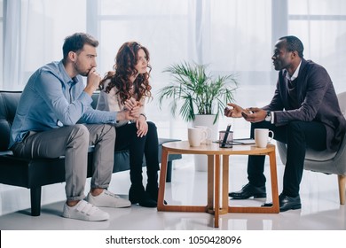 Smiling african american psychiatrist talking to young couple in office
