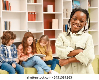 Smiling African American schoolboy with folded hands looking at camera in the library while his classmates reading books on the background - Powered by Shutterstock