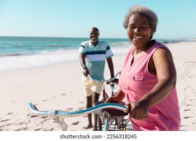Smiling african american senior couple with bikes walking on sandy beach under clear sky in summer. Copy space, travel, unaltered, vacation, love, together, retirement, nature and active lifestyle. . - Powered by Shutterstock