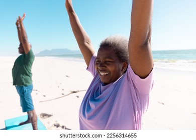 Smiling african american senior woman and man raising arms and exercising at beach against clear sky. Copy space, unaltered, love, together, yoga, retirement, nature, vacation and active lifestyle. - Powered by Shutterstock