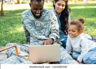 Smiling African American Soldier In Military Uniform Using Laptop With Family In Park