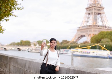 Smiling African American taking selfies on background of Eiffel Tower using silver smartphone. Young woman came to Paris for honeymoon. Black-haired woman with beautiful hair styling wearing
