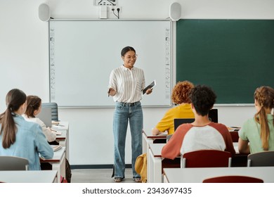 Smiling african american teacher with digital tablet talking to pupils during lesson in class