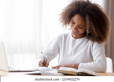 Smiling African American Teen Girl Preparing School Homework, Using Laptop, Happy Black Schoolgirl, Pupil Doing Tasks, Writing Essay, Studying At Home, Making Notes, Writing, Reading Textbooks