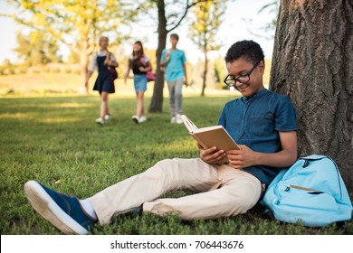 smiling african american teenage boy in eyeglasses studying in park
