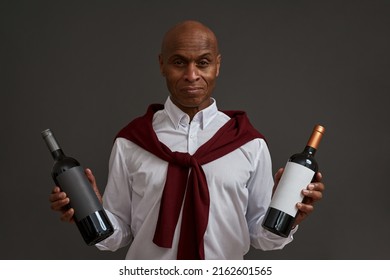 Smiling african american winemaker or sommelier holding two wine bottles. Adult successful male entrepreneur. Viticulture and winemaking. Isolated on grey background. Studio shoot. Copy space - Shutterstock ID 2162601565