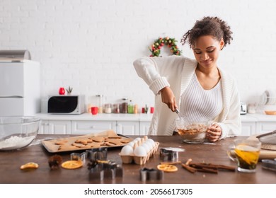 Smiling African American Woman Cooking Near Ingredients And Christmas Cookies In Kitchen