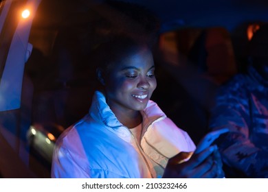 Smiling African American Woman Holding Smartphone Using Social Media App, Reading Blog Posts While Sitting In Car With Boyfriend. Female Blogger Sharing News Online. Cellphone Addiction And Nomophobia