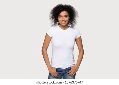 Smiling African American woman in jeans and blank white t-shirt front mock up, attractive young female demonstrate clothes design template copy space for print, isolated on studio background