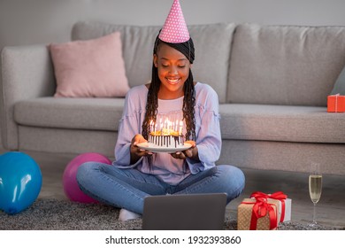 Smiling African American Woman In Party Hat Showing Her Online Friend Cake, Celebrating Birthday Online During Self-isolation, Happy Black Lady Having Video Conference With Family Or Boyfriend