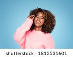 Smiling african american woman in pink sweater and eyeglasses posing on blue studio background .