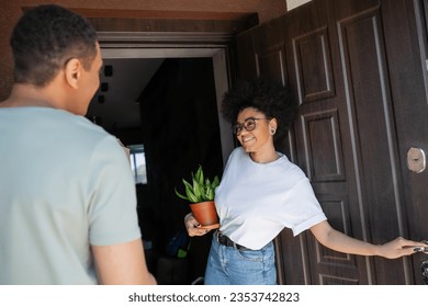 smiling african american woman with plant opening door of new house near blurred boyfriend - Powered by Shutterstock