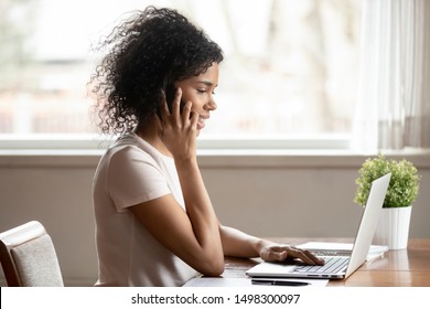 Smiling African American Woman Sit At Table At Home Multitask Work At Laptop Talk On Cellphone, Happy Biracial Female Use Computer Have Pleasant Smartphone Call Conversation, Technology User Concept