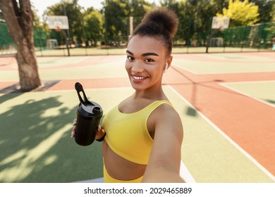 Smiling African American woman taking selfie using cellphone gadget, millennial sports influencer recording video blog. Positive black lady holding shaker taking break standing outside at sports field - Powered by Shutterstock