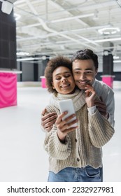 Smiling african american woman touching boyfriend and taking selfie on smartphone on ice rink  - Shutterstock ID 2232927981