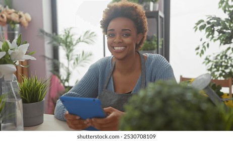 Smiling african american woman using tablet in an indoor flower shop surrounded by lush greenery. - Powered by Shutterstock