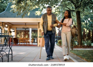 Smiling African American Woman Walking With Her Senior Father While Visiting Him At Nursing Home.