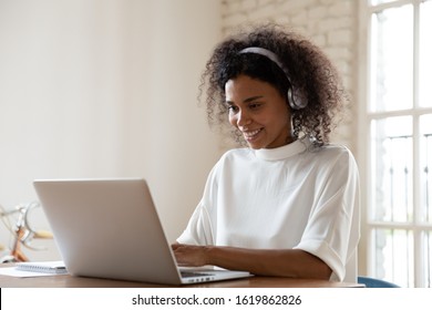 Smiling African American Woman Wearing Headset Using Laptop In Modern Office, Looking At Screen And Typing, Listening To Music, Interpreter Working Online, Learning Computer Course, Lecture