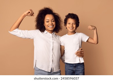 A smiling African American woman and a young boy are flexing their muscles together, showcasing a bond of strength and confidence. - Powered by Shutterstock