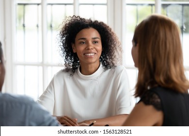 Smiling african american young businesswoman talking with diverse clients or partners at business meeting in office. Happy mixed race female hr manager conducting job interview with applicants.