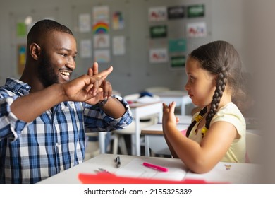 Smiling african american young male teacher teaching sign language to caucasian elementary girl. unaltered, education, childhood, learning, teaching, disability and school concept. - Shutterstock ID 2155325339