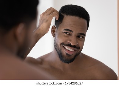 Smiling african American young man look in mirror in bathroom get ready in morning, happy biracial millennial male style hair, do daily beauty procedures treatment in bath, haircare concept - Powered by Shutterstock