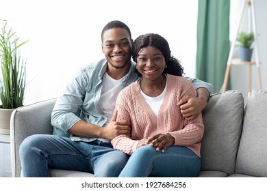 Smiling African American Young Man And Woman Posing On Sofa At Home, Spending Weekend Together, Copy Space. Cheerful Black Family Embracing While Relaxing On Couch In Living Room