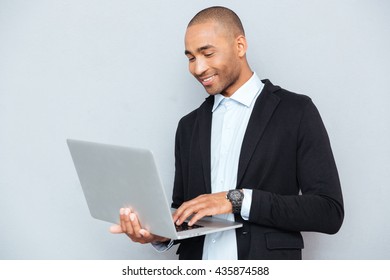 Smiling African American Young Man Standing And Using Laptop