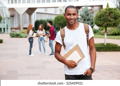 Smiling african american young man student with backpack standing outdoors
