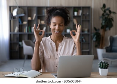 Smiling African American young woman with closed eyes meditating, sitting at desk with laptop, mindful happy businesswoman freelancer or student enjoying break, practicing yoga, stress relief concept - Powered by Shutterstock