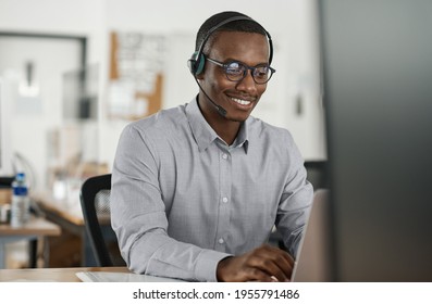 Smiling African businessman talking on a headset and using a laptop
