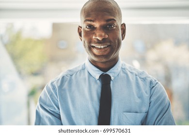 Smiling African businessman wearing a shirt and tie standing alone in front of a window in his home office - Shutterstock ID 699570631