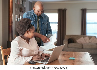 Smiling African couple paying bills and doing their online banking with a laptop at their kitchen table at home