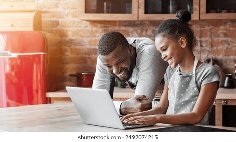 Smiling african daddy and daughter looking for nice recipe, using laptop at kitchen, empty space - Powered by Shutterstock